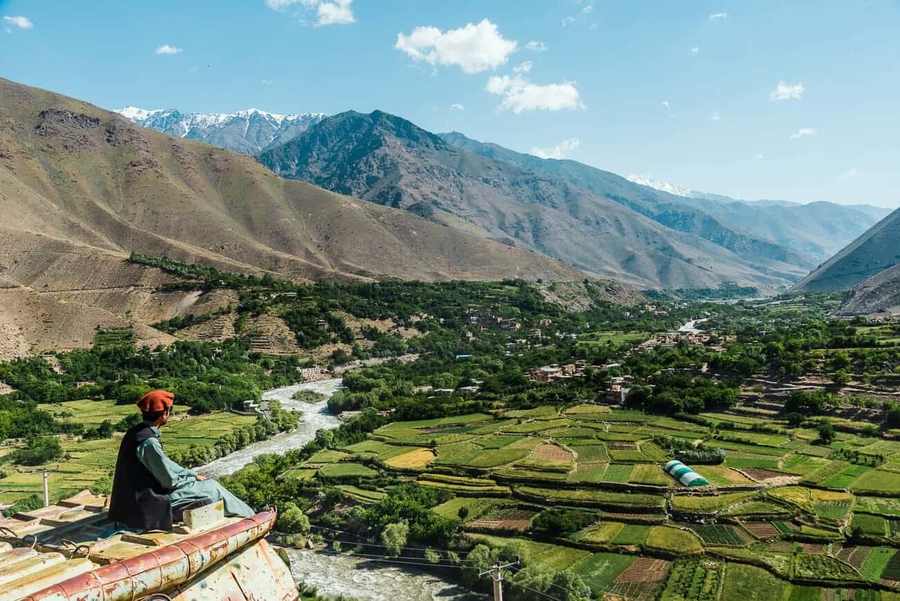 A man in a pakol and shawl seen from behind, overlooking a terraced river valley