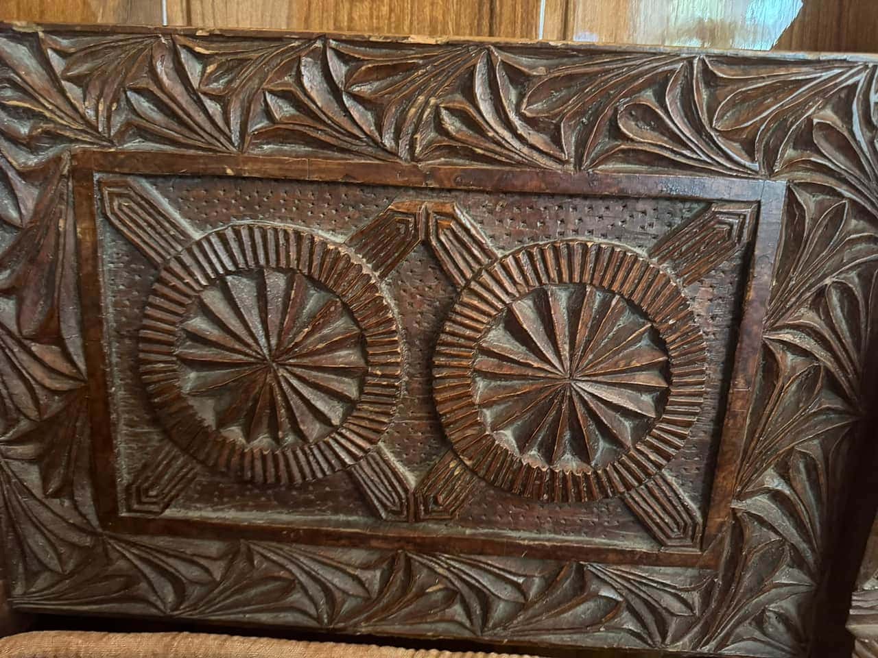 Two carved rosettes on the back of a Nuristani chair, framed by a leaf border