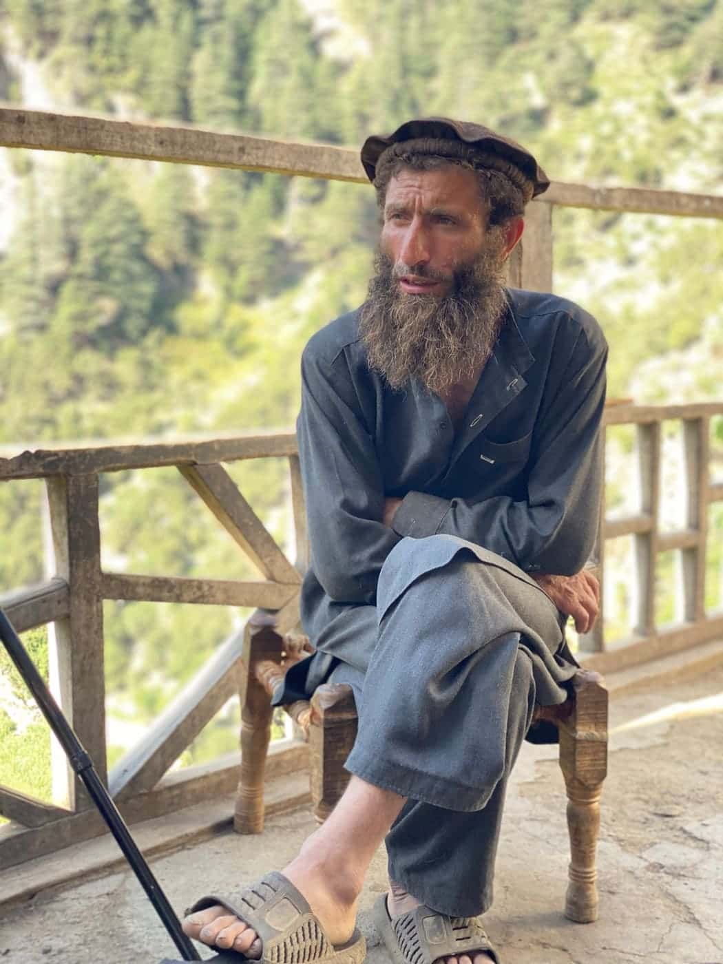 A Nuristani elder seated on a hand-turned wooden stool on a timber veranda