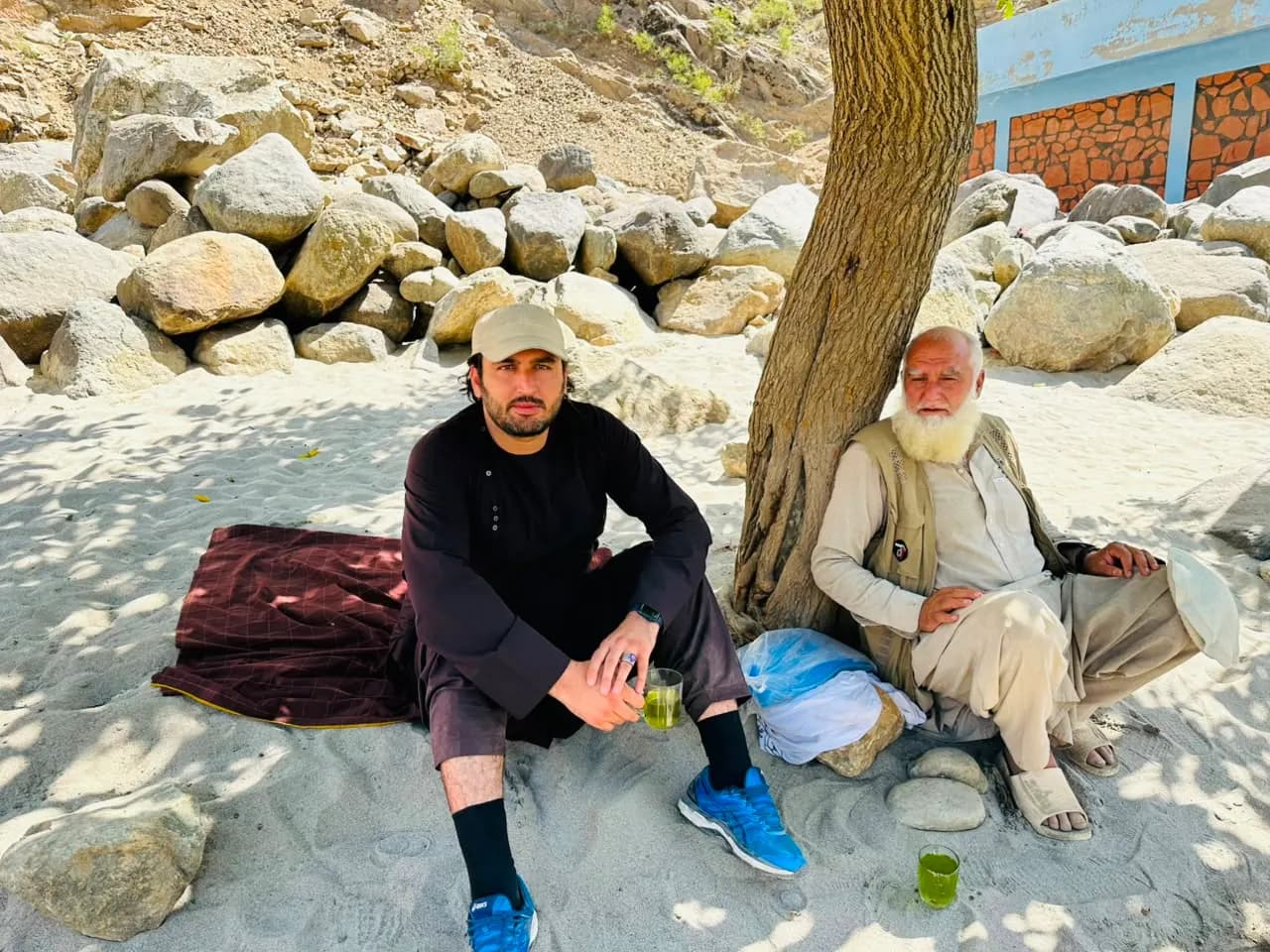 Abdulrahman Chonish and an elder drinking green tea in the shade of a tree on river sand