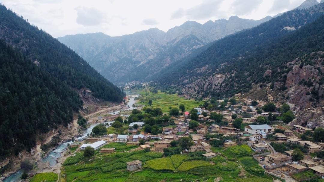 A village of timber houses above a river and terraced fields, seen from above