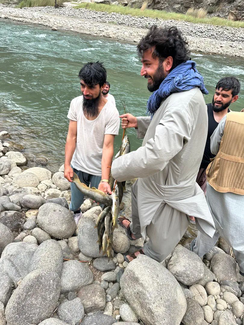 Abdulrahman Chonish and local men on the stony bank of the Dani Pajagal river in Du Ab, holding up strings of freshly caught fish