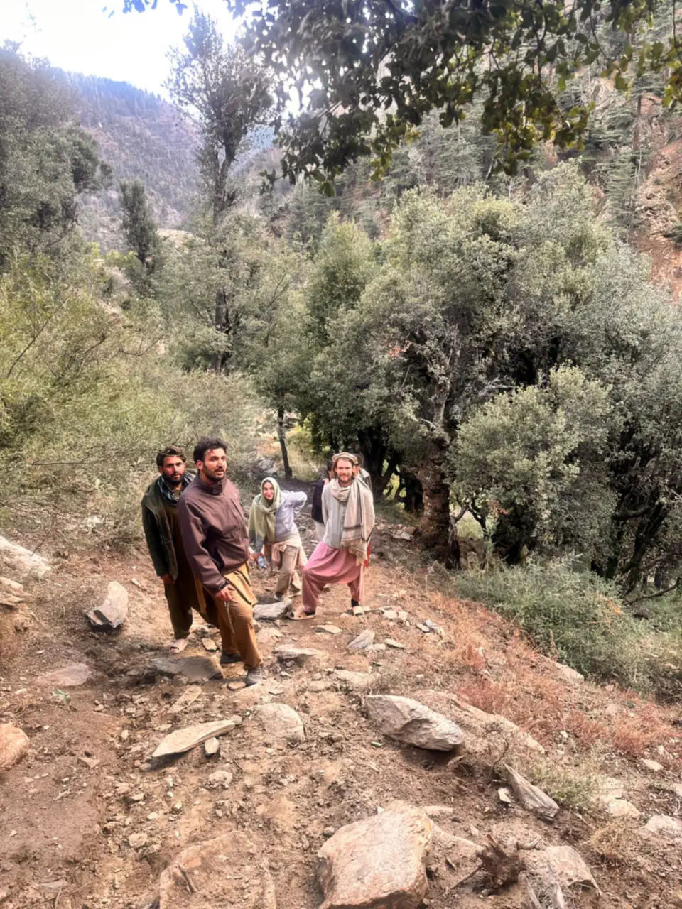 Abdulrahman Chonish leading a hike up a stony path through the woods of the Sewketra valley in Waygal, a local man beside him and two guests from the Netherlands behind
