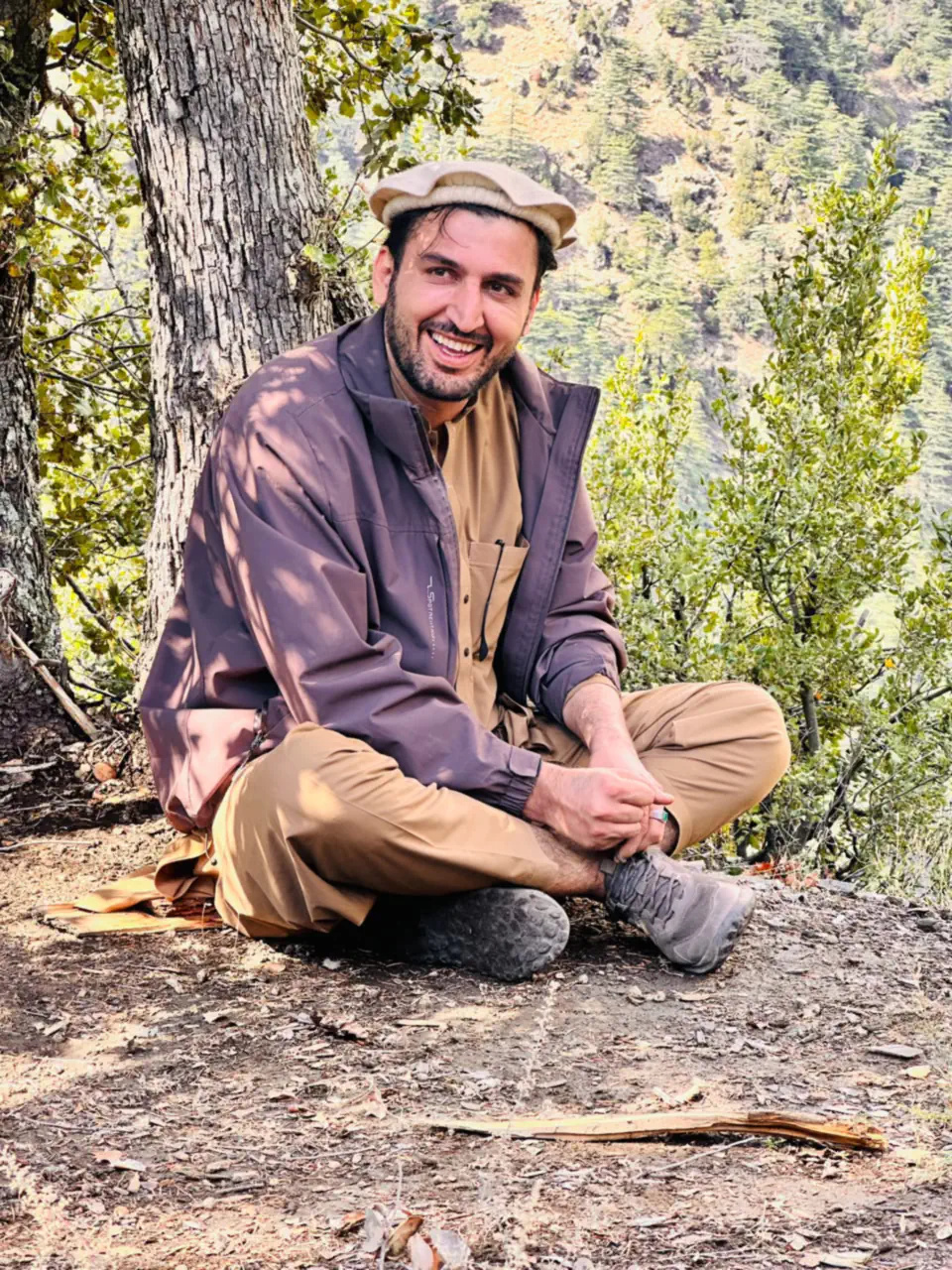 Abdulrahman Chonish in a cream wool pakol rolled at the brim, sitting under a tree in the Sewketra valley of Waygal, Nuristan