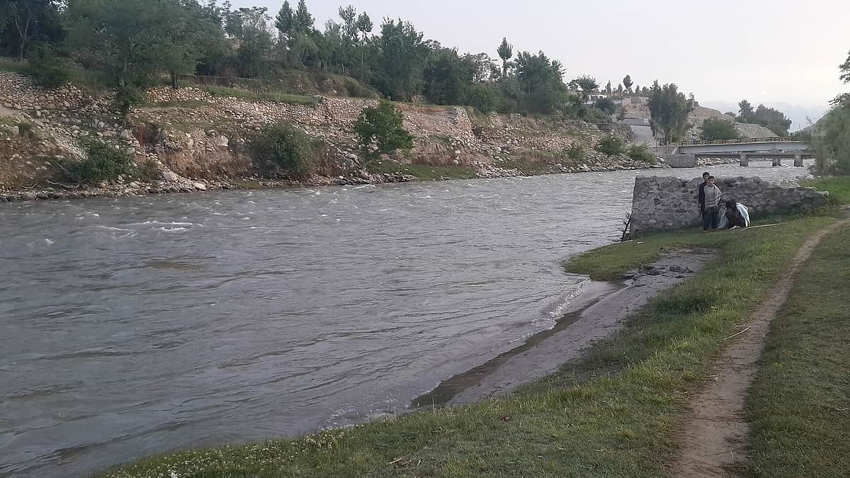 The Alingar river running wide and shallow between stony banks and green fields in Laghman