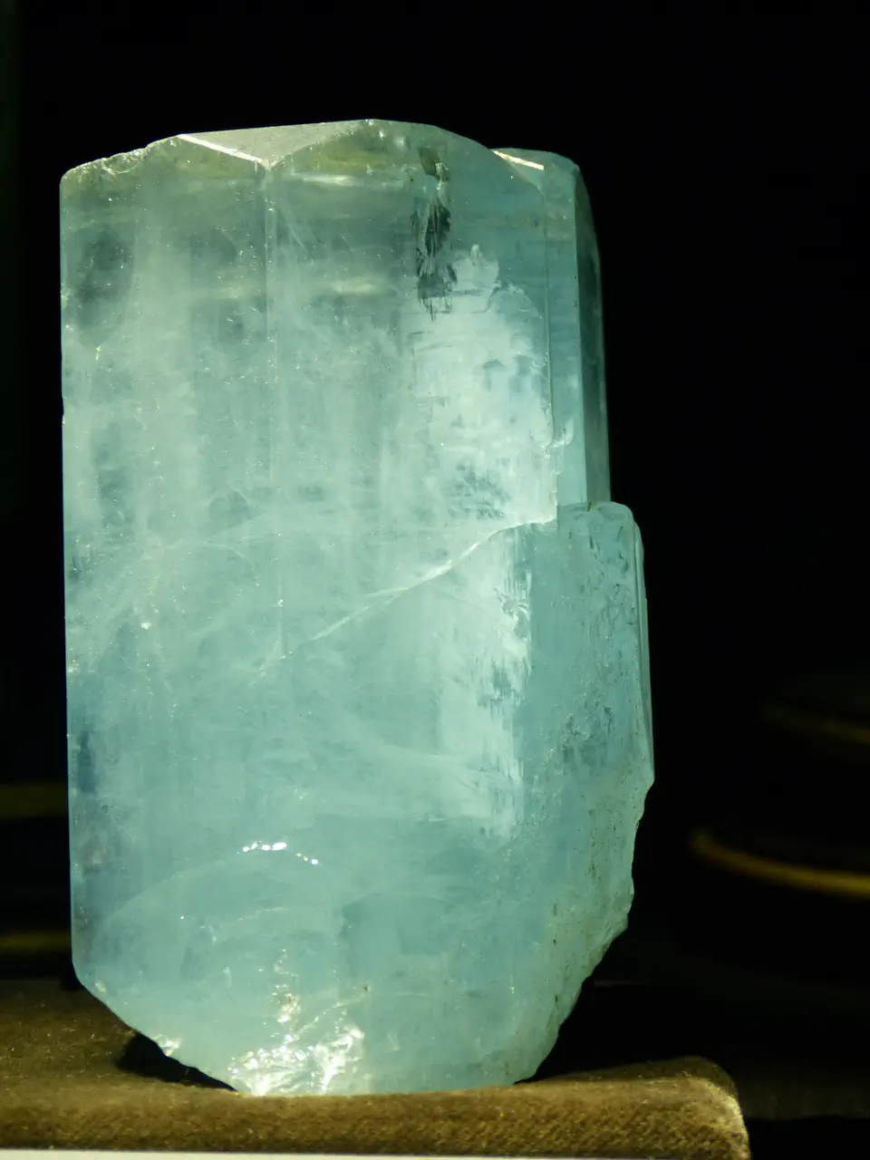 A large glassy blue aquamarine crystal from Afghanistan lit against a dark background in the Natural History Museum, Vienna