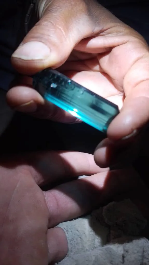 A blue tourmaline crystal, indicolite, from the Yinshaw valley in Waygal, Nuristan, lit from behind by a torch and glowing deep blue-green in a cupped hand