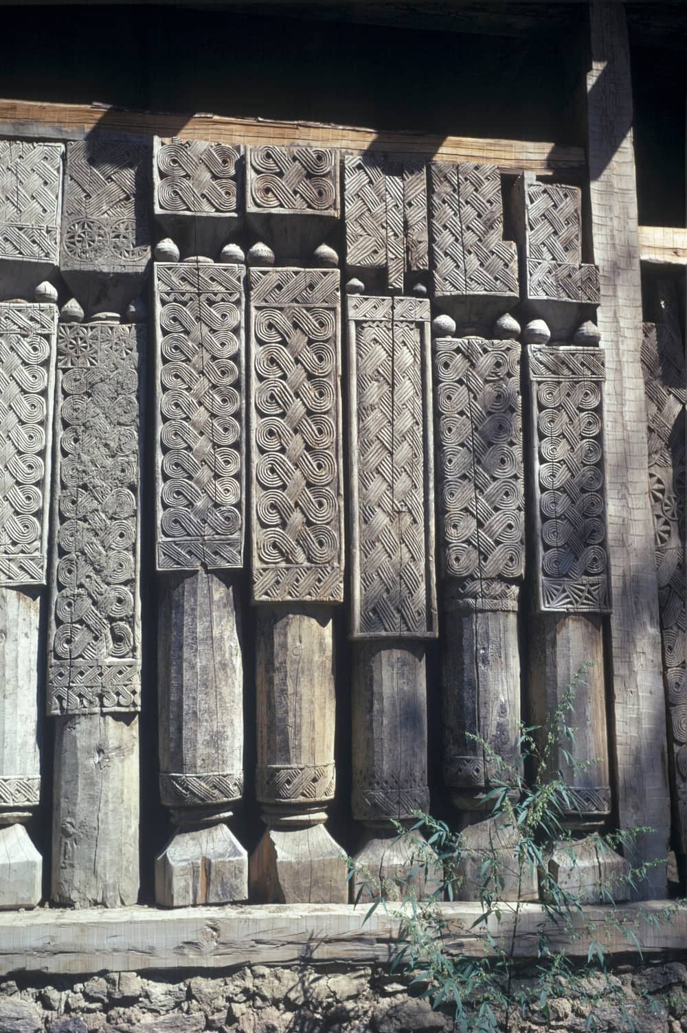 A wall of broad timber plank-columns at the Kamdesh mosque, each carved from top to bottom with interlaced knots and plaits, photographed in colour in 1968