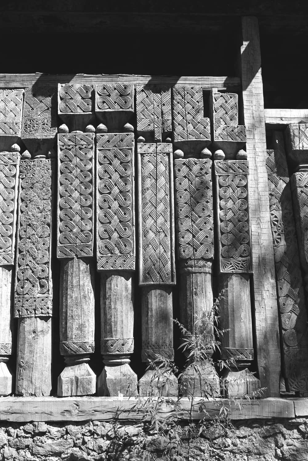 A black and white photograph of timber pillars carved with interlaced knots and rosettes on the front of a mosque near Kamdesh