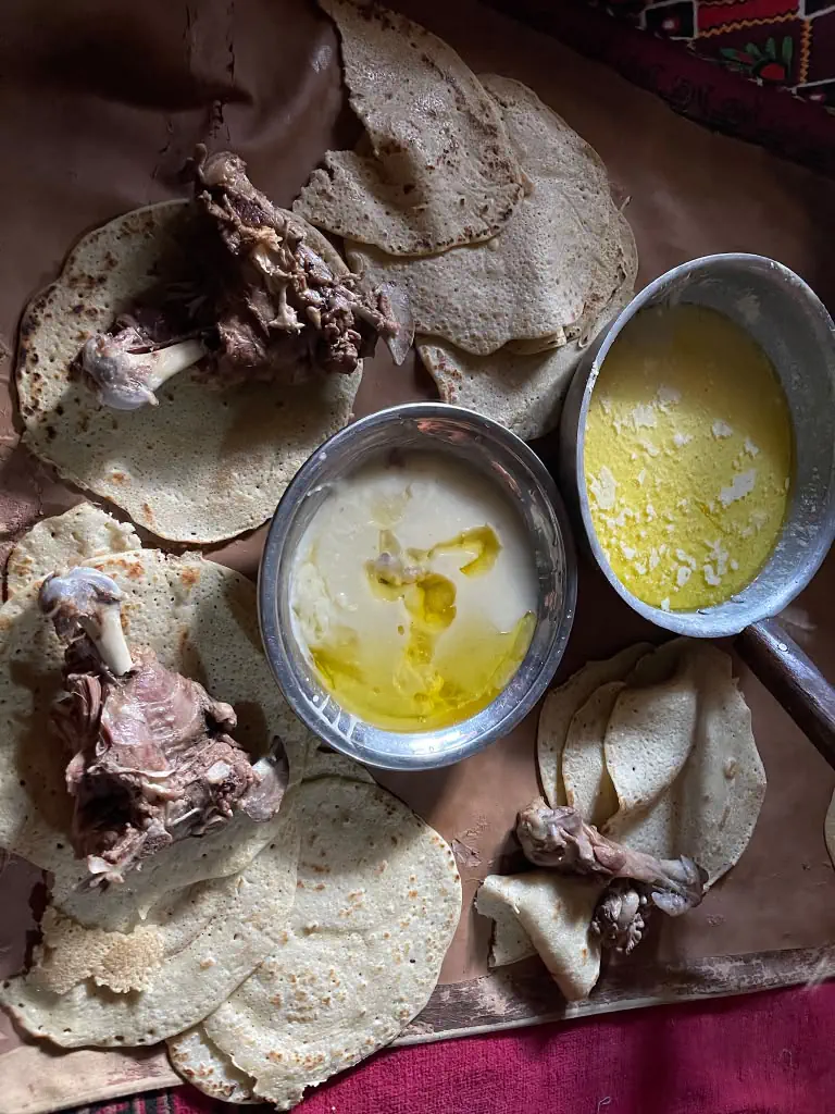 A traditional meal in Kantiwa laid out on a cloth: flat bread, meat on the bone, a bowl of dried yoghurt with melted butter, and a pan of butter