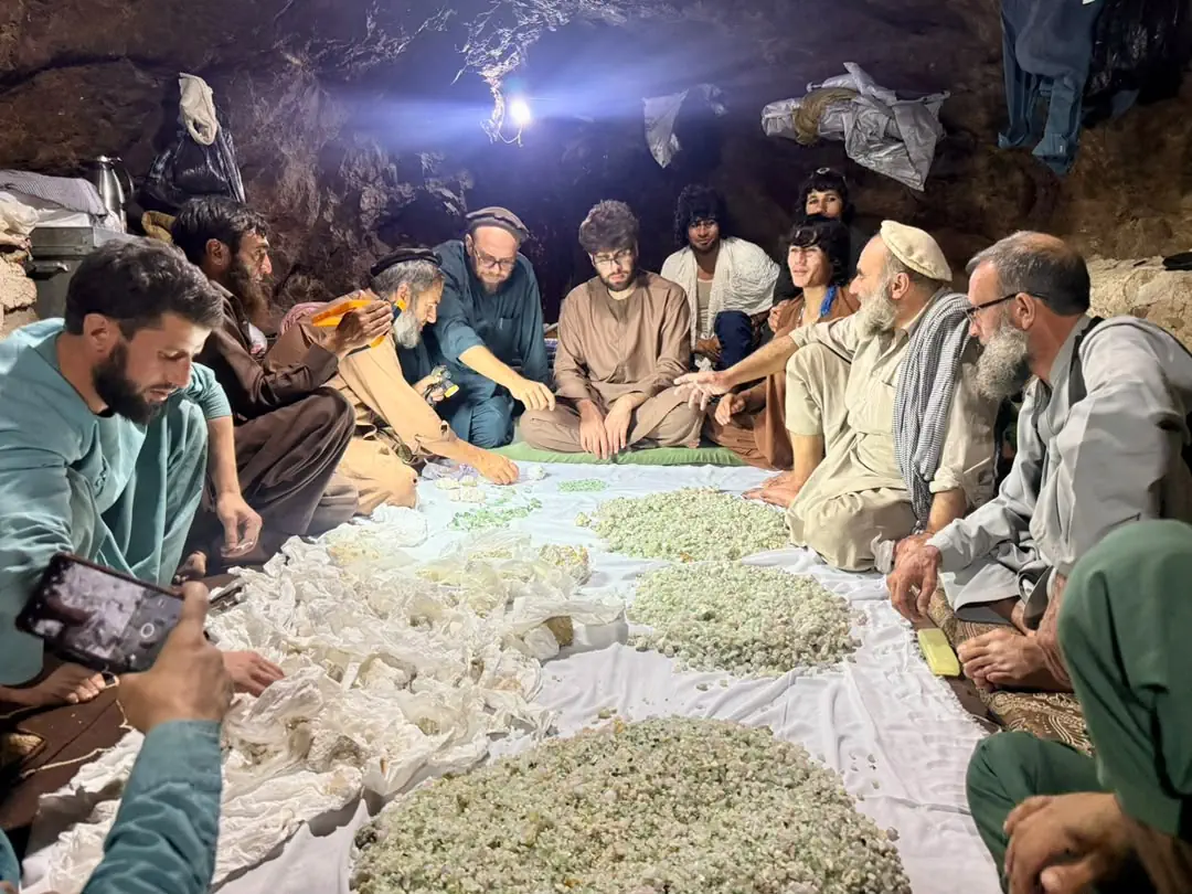 Miners and traders seated round a white cloth inside the Mawi mine in Du Ab, Nuristan, sorting heaps of rough tourmaline and tissue-wrapped specimens under a single lamp