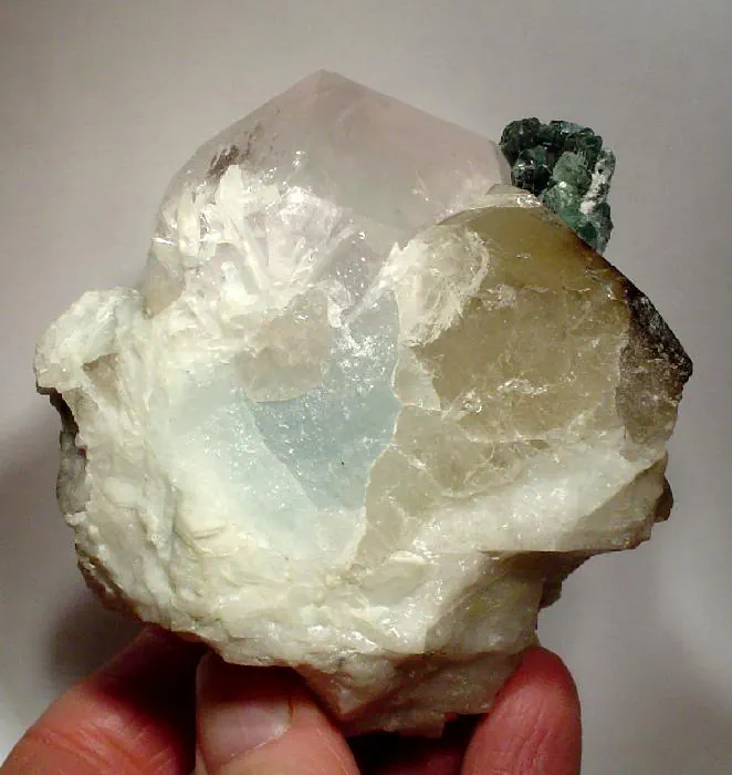 A pocket piece from Kunar province, Afghanistan: a pale morganite crystal with a blue aquamarine core beside green indicolite tourmaline and colourless spodumene on white albite