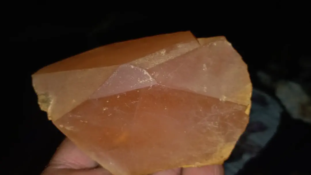 A rough morganite crystal from the Sewketra valley in Waygal, Nuristan, peach to orange-brown with flat faces, held in a hand against a dark background
