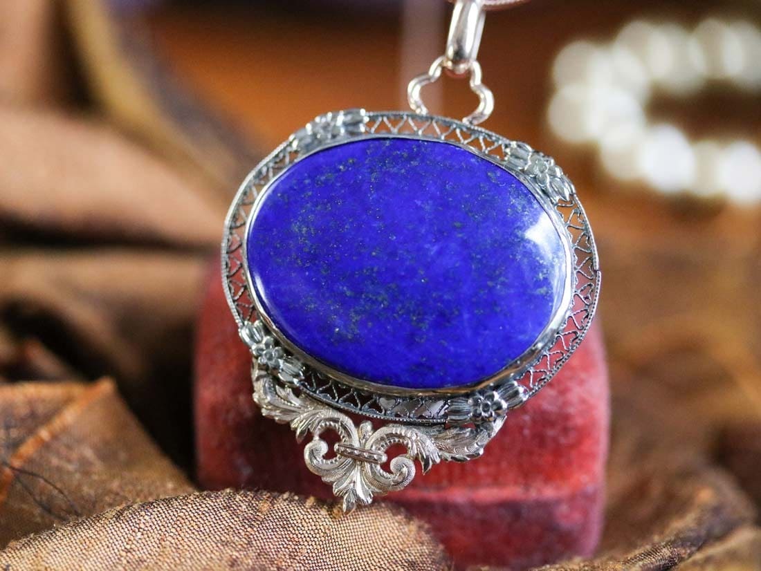 A polished lapis lazuli cabochon set in an ornate silver filigree pendant