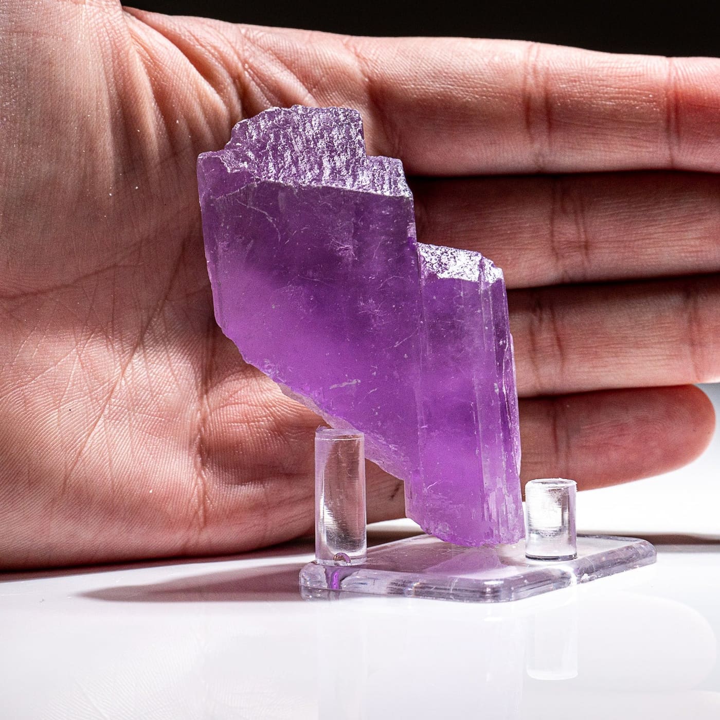 A lilac kunzite crystal from Nuristan displayed on a stand in front of an open hand