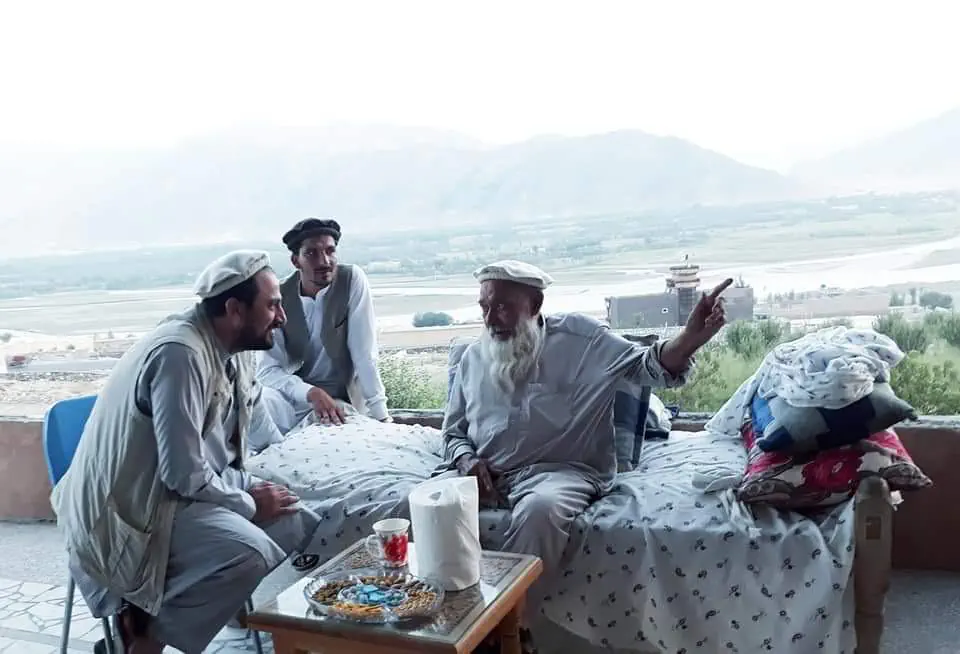 Obaid Nuristani with an elder and a tribal leader of Kunar on a terrace, the white-bearded elder pointing out over a wide river plain