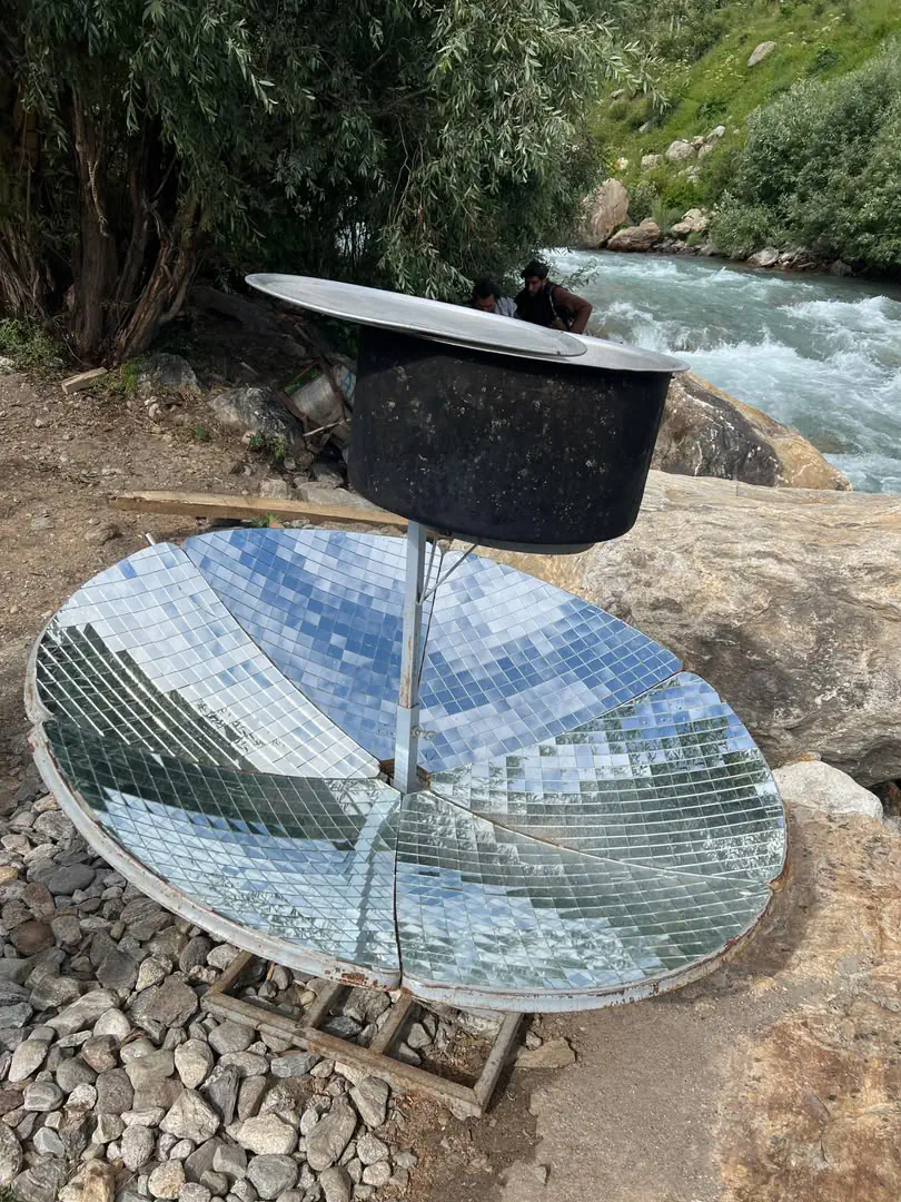 A solar cooker beside the river in Parun: a dish lined with mirror tiles focusing sunlight on a blackened cooking pot
