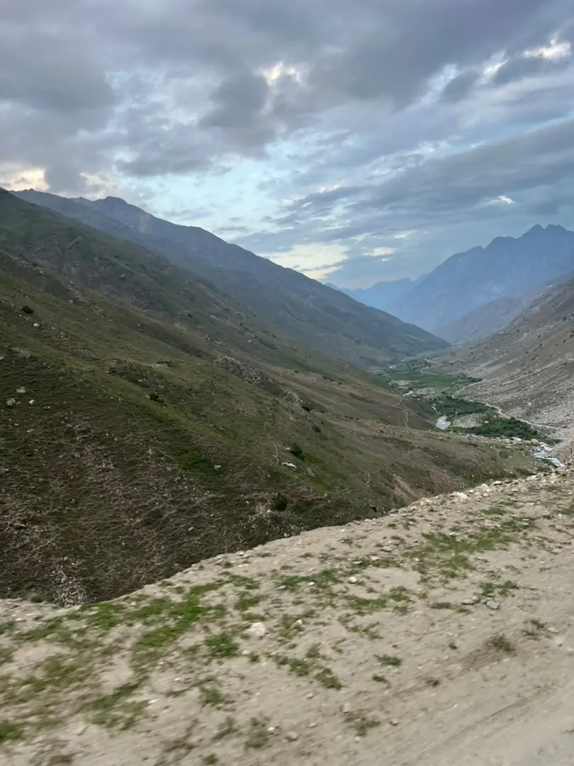 Bare grass slopes above a river in Parun under grey cloud, the river threading the valley floor