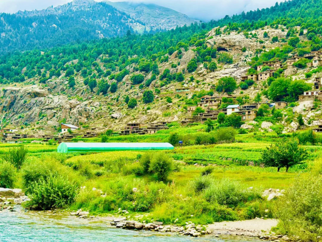 Stone and timber houses terraced up a hillside above the Parun river, green fields and a long polytunnel on the valley floor