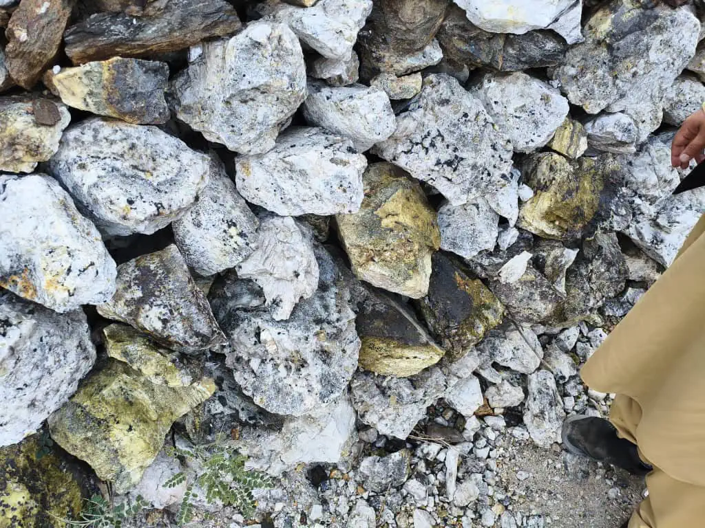 Pale rock speckled with black crystals and yellow-green stones on a slope in the Pashagar valley, Nurgaram, where the stones point to gemstones nearby
