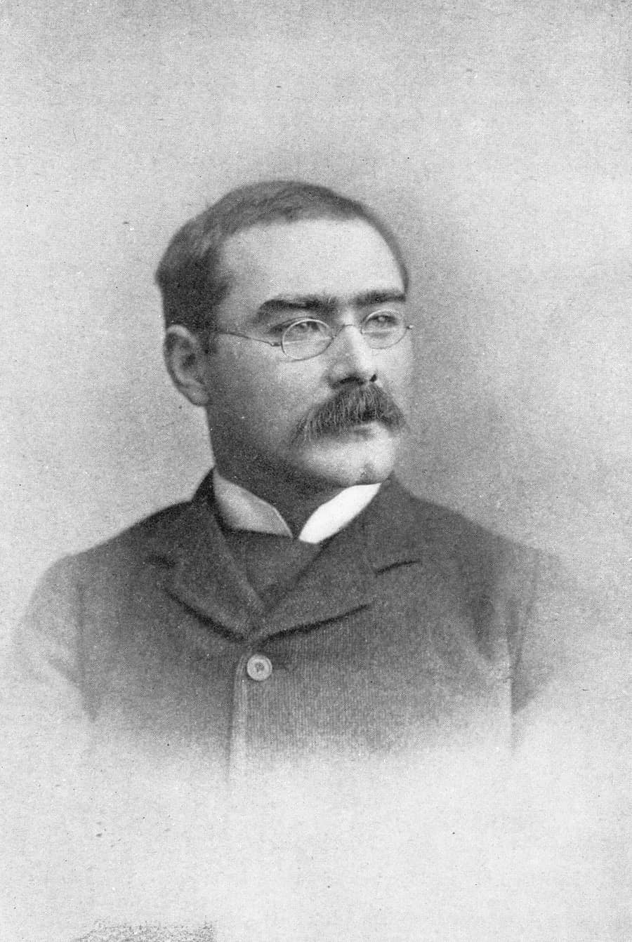 A studio portrait of Rudyard Kipling in 1895, with round spectacles and a heavy moustache, signed at the foot