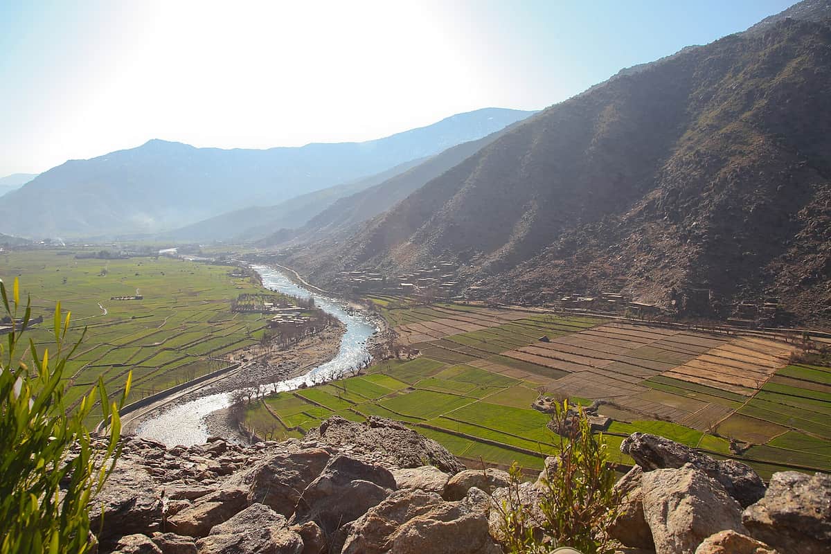 The Pech river winding between terraced fields and a stone village in Watapur district, mountains behind