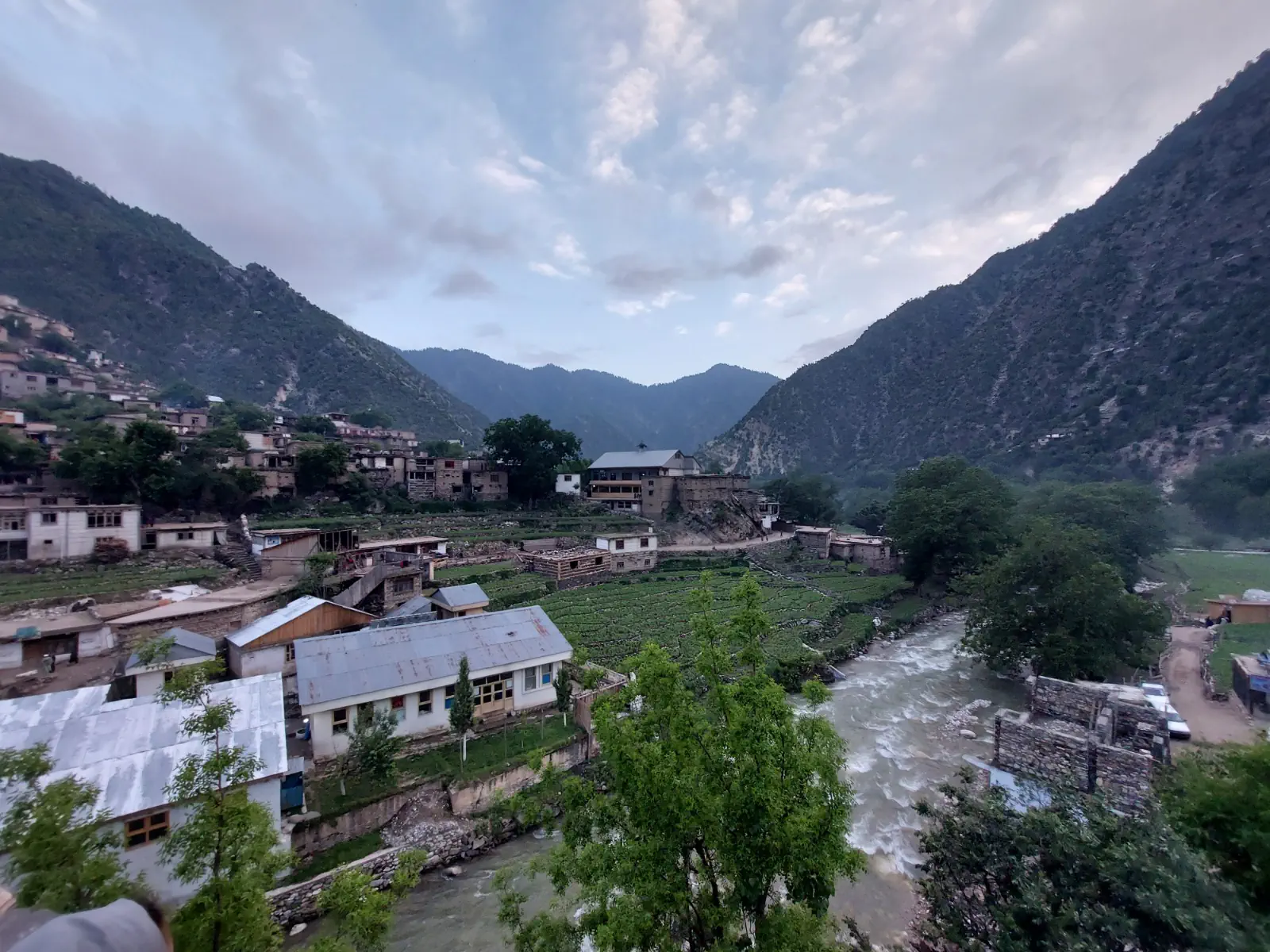 The centre of Waygal district from above: houses, terraced fields and the Waygal river between forested mountains